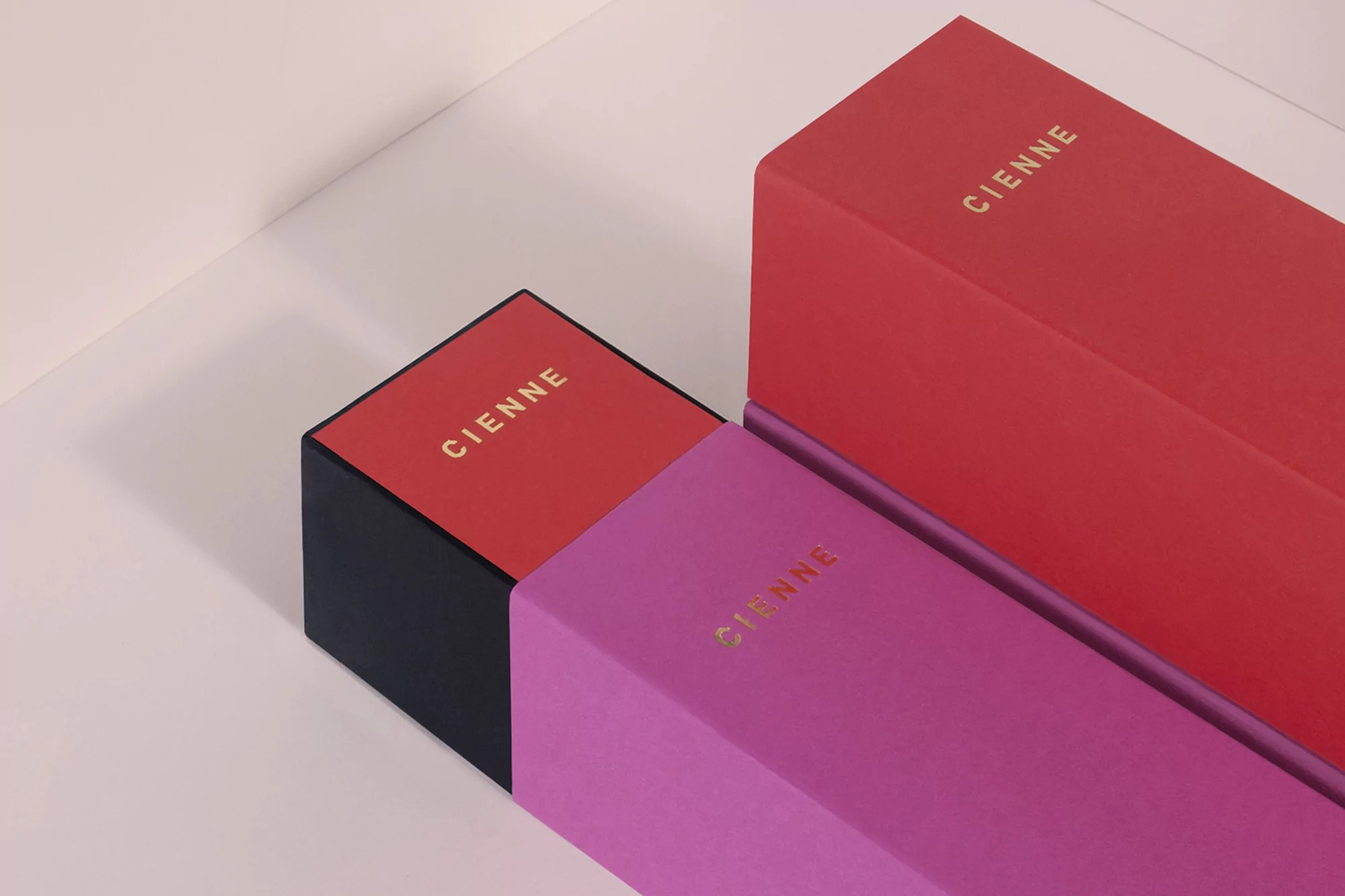 Arrangement of Cienne branded red, pink, and black cardboard boxes in a product shot with studio lighting against a neutral background.