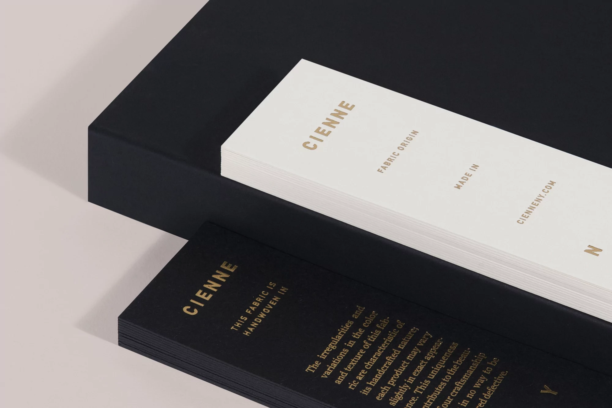 Stacks of black and white Cienne fabric origin cards, displaying brand name, 'Fabric Origin,' 'Made In,' and website on a layered surface.
