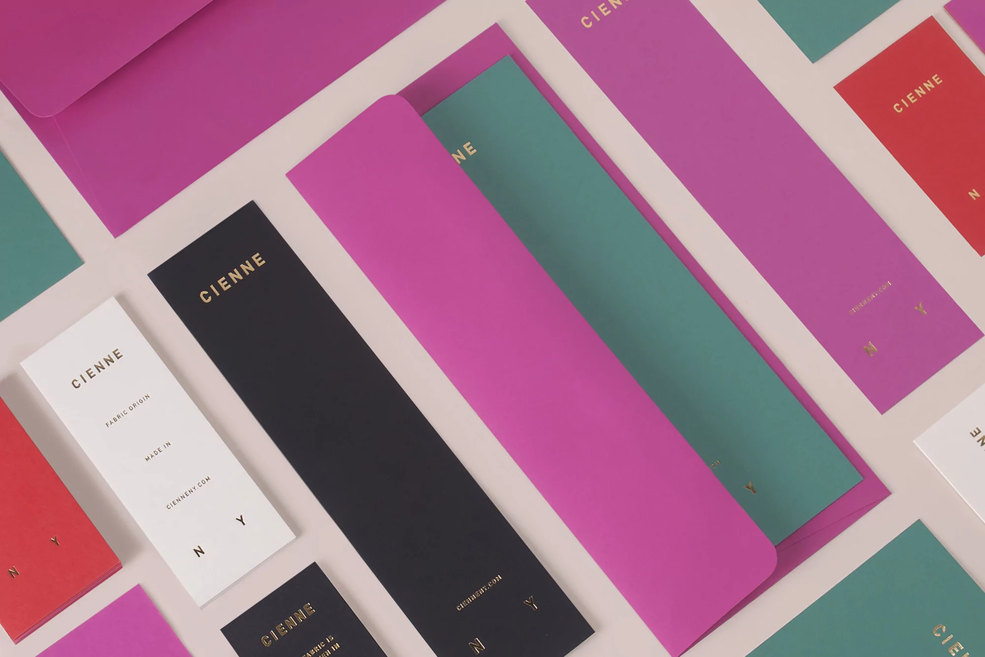 Cienne brand identity stationery including magenta envelopes, black tags, and teal cards arranged on a light background