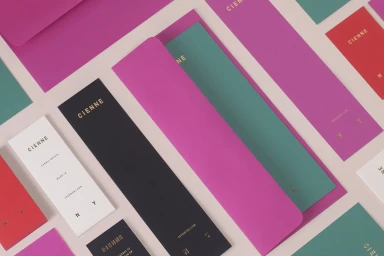 Cienne brand identity stationery including magenta envelopes, black tags, and teal cards arranged on a light background