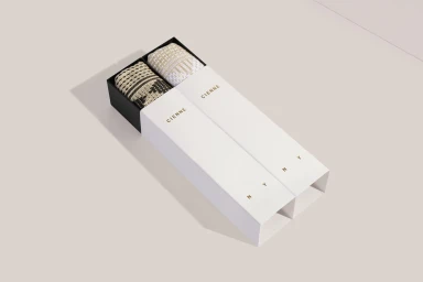 Two rolled patterned scarves displayed inside white branded packaging boxes on a pale neutral surface