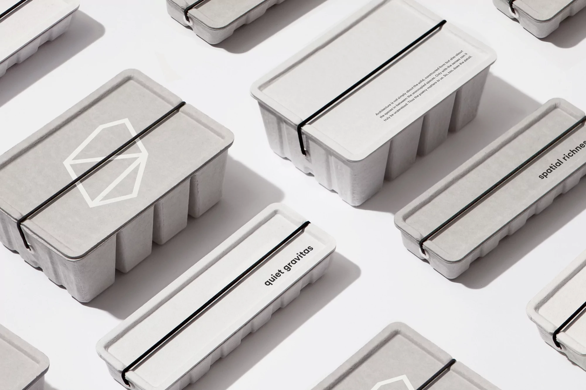 Several white rectangular boxes with lids are arranged on a white surface, each secured with a black band. Text is visible on the lids.