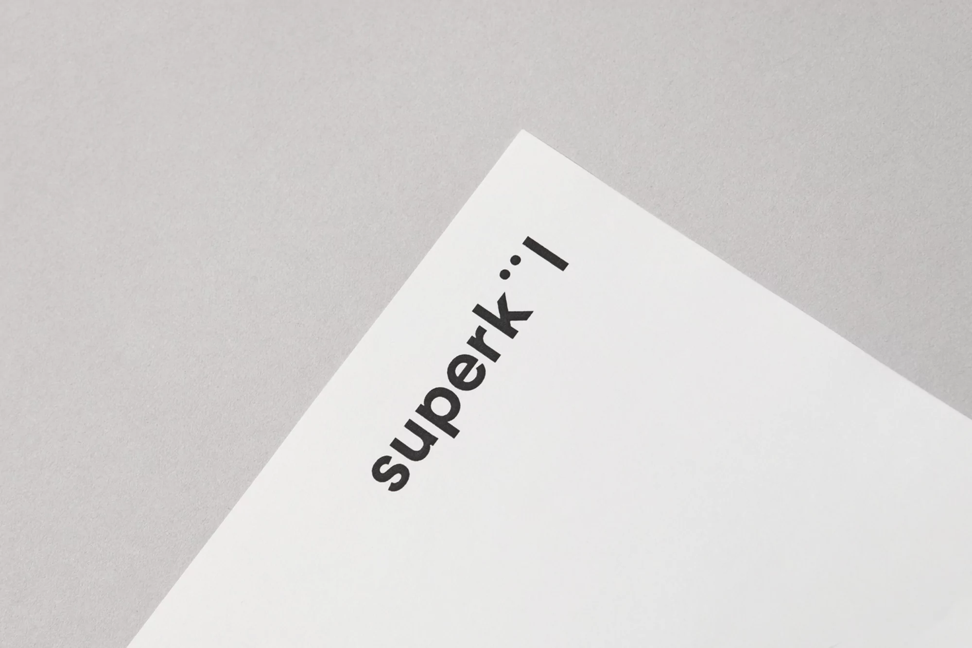 Close-up shot of a white paper surface with the text 'superk' printed in black ink, creating a minimalist aesthetic with neutral tones.
