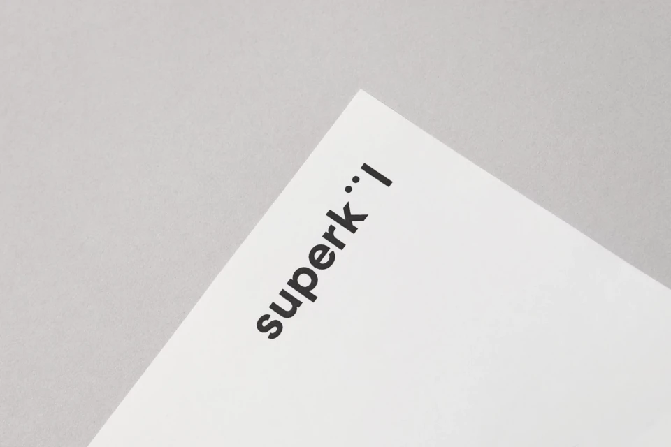 Close-up shot of a white paper surface with the text 'superk' printed in black ink, creating a minimalist aesthetic with neutral tones.