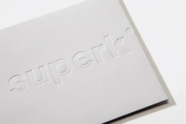 Close-up of a white textured paper card featuring a debossed SuperKul brand logo against a plain background