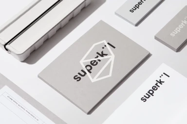 Minimalist stationery layout displaying the SuperKul brand identity with grey cards and white paper on a white surface.