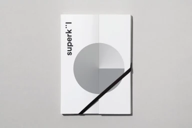 Folded white brochure with geometric grey circle graphics and black diagonal elastic band on grey surface