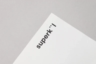 Close-up angled shot of the SuperKul brand name printed in black uppercase typography on a white paper card against a grey background.