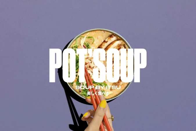 Overhead shot of pot soup with sliced chicken and vegetables, served with chopsticks held by a manicured hand against a purple backdrop.