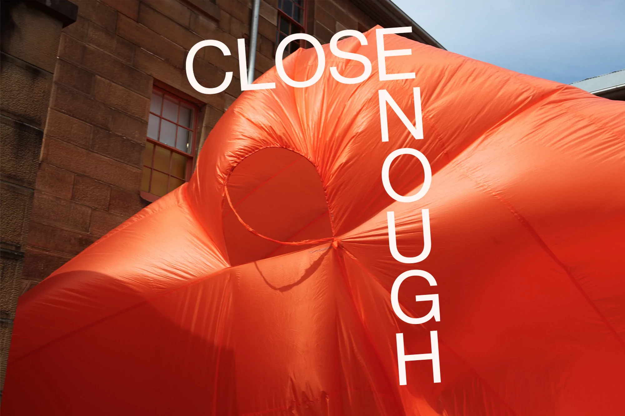 Bright orange inflatable structure partially fills the frame, set against a stone building exterior under a clear, daytime sky.