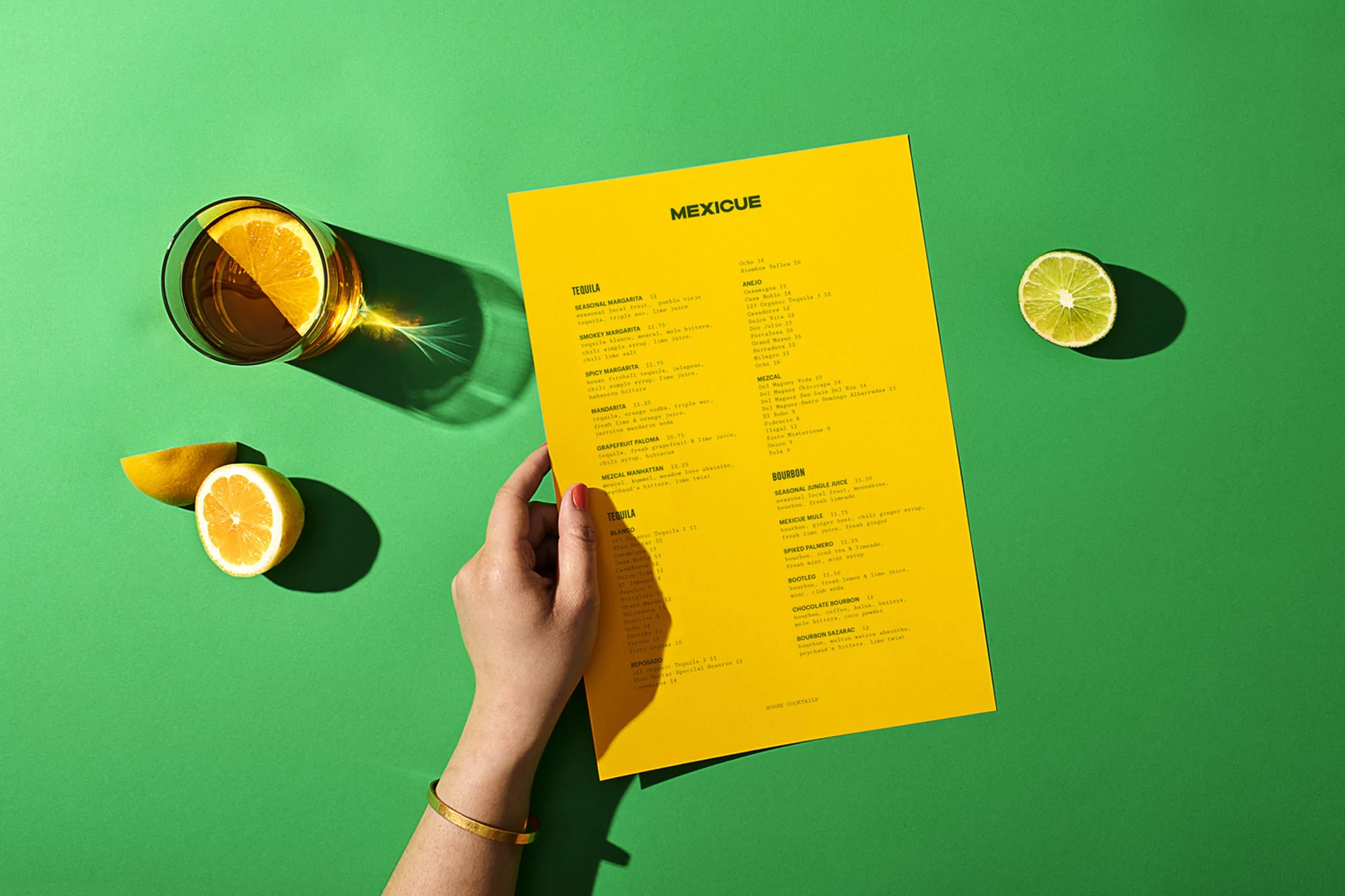 Overhead shot of a woman holding a menu, with a drink, citrus fruit slices on a green background, highlighting a culinary experience.