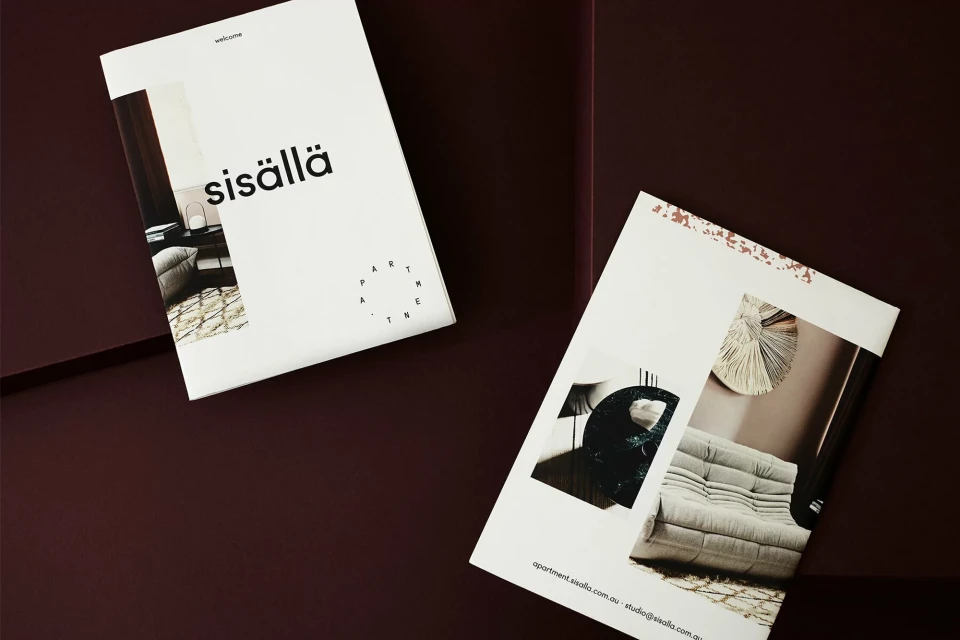 Two 'sisällä' magazines on a plum surface. One magazine lies flat, and the other is leaning, showing an interior design photo.