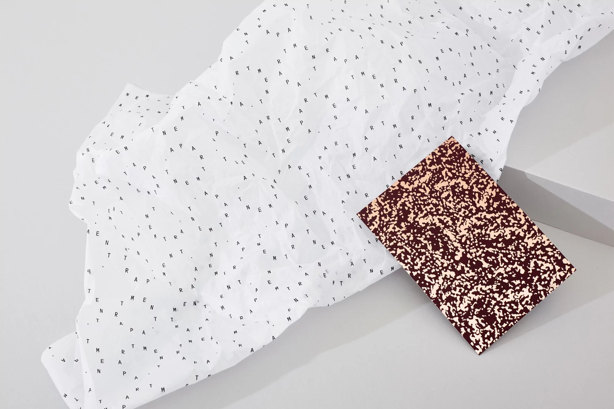 Stylish product flat lay featuring a brown speckled notebook on a white patterned paper, creating a minimalist studio aesthetic.