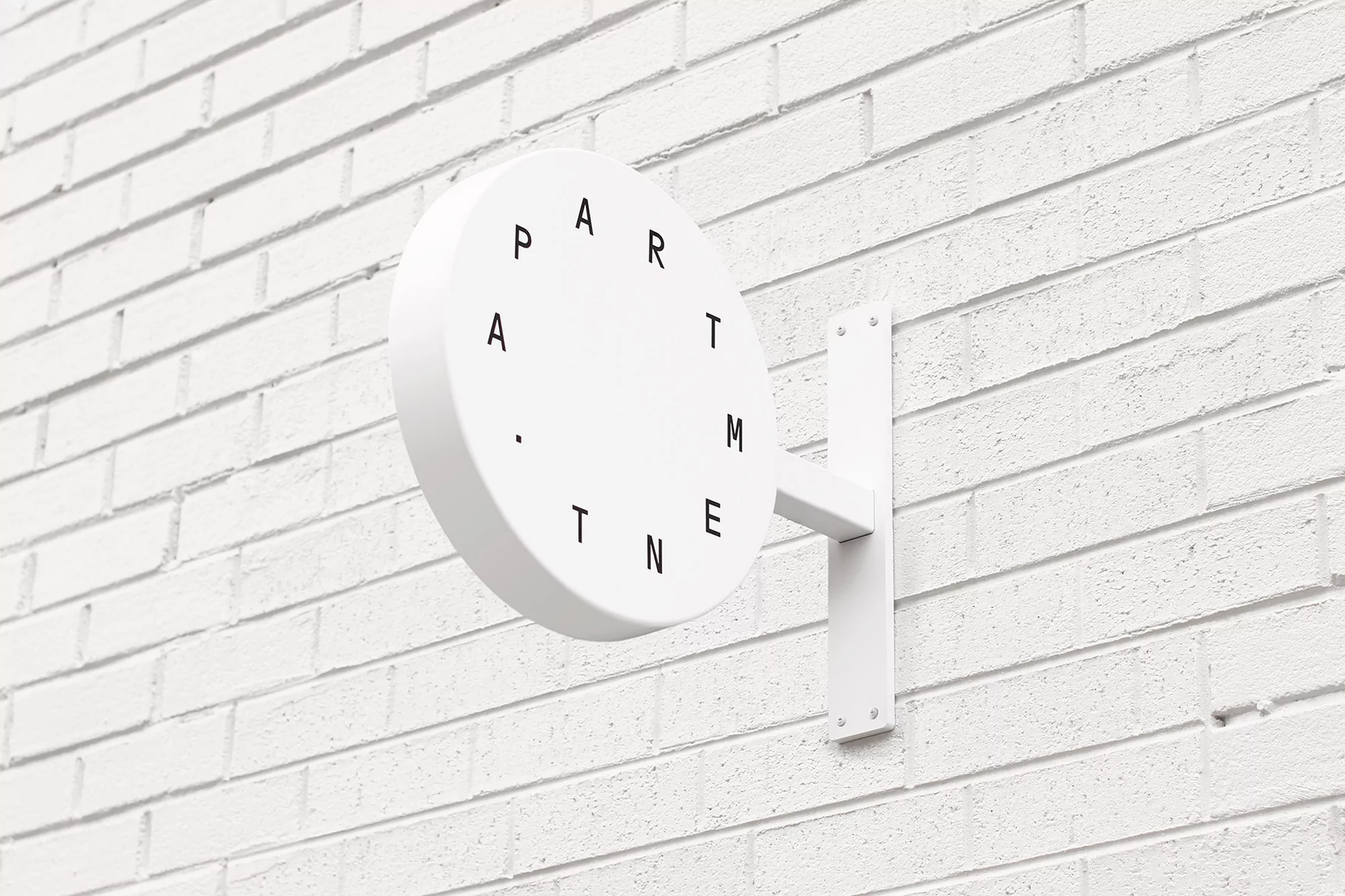 Exterior shot of a white circular sign with the word 'APARTMENT' in a circular pattern, mounted on a textured white brick wall.
