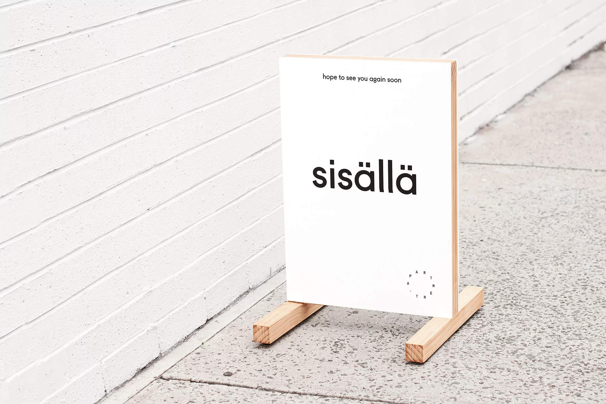 Minimalist sign with 'sisällä' in black letters, set against a white wall and light gray pavement; promotes a shop or event.