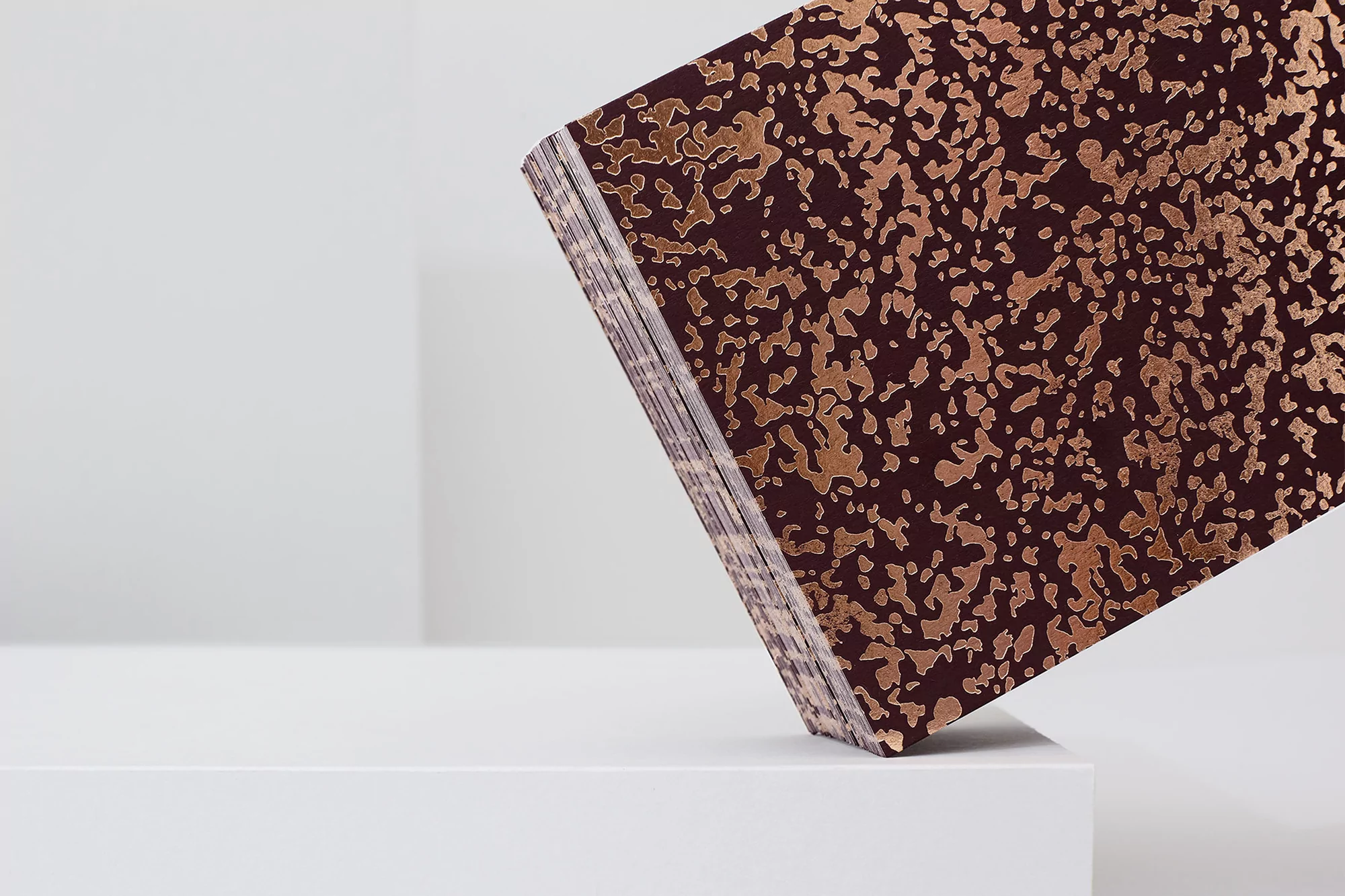 Stack of maroon paper with gold abstract pattern on a white surface, set against a plain white background, creating a minimalist composition.