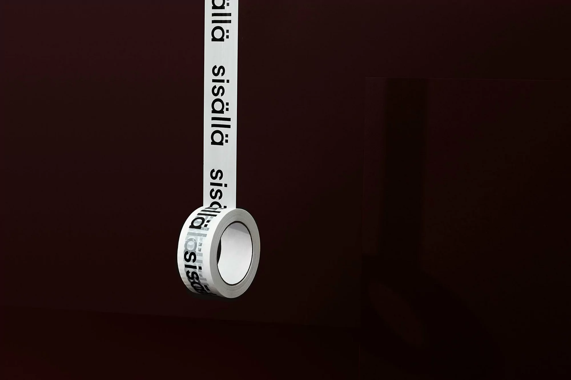 Roll of white tape with black text 'sisällä' unspooling against a dark gradient background in a studio shot with simple lighting.