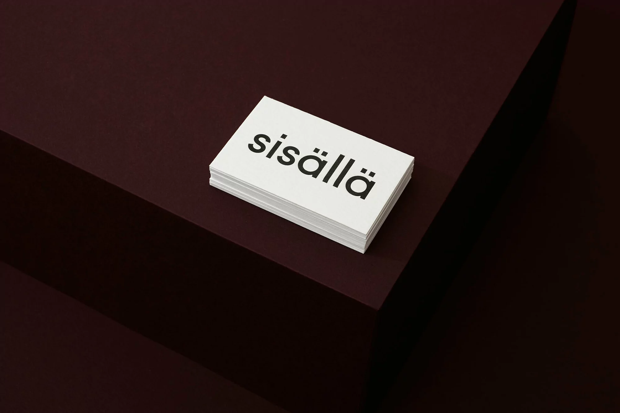 Stack of white business cards with black text on burgundy surface. Minimal design concept for corporate identity and branding.