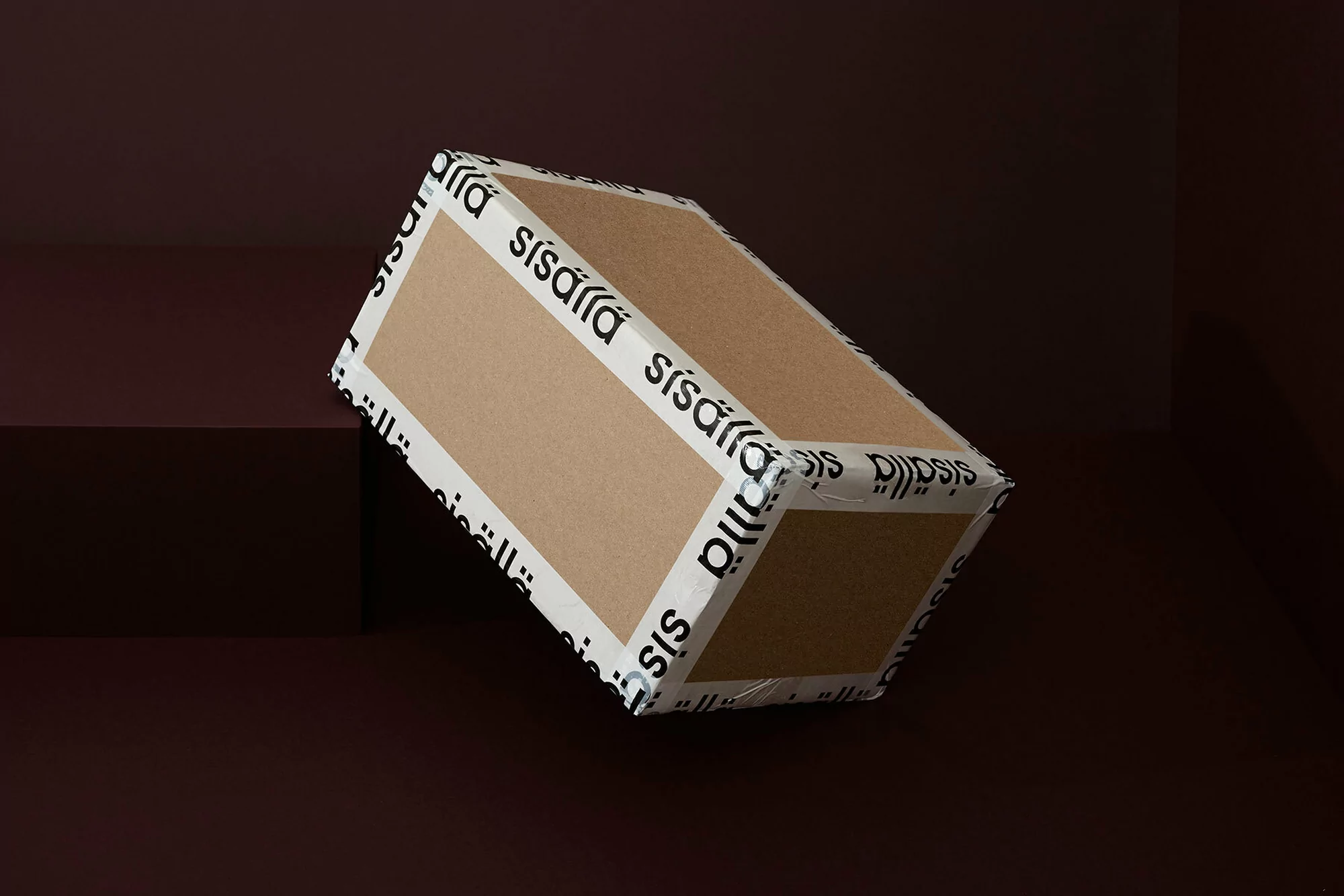 Brown cardboard box with branded white tape is angled on a dark brown surface with a matching background, simple modern product shot.