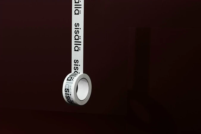 A roll of white tape printed with Finnish text hanging vertically against a dark brown background.