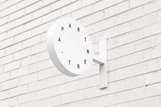 White circular wall-mounted sign with black typography reading apartment mounted on a white brick wall exterior
