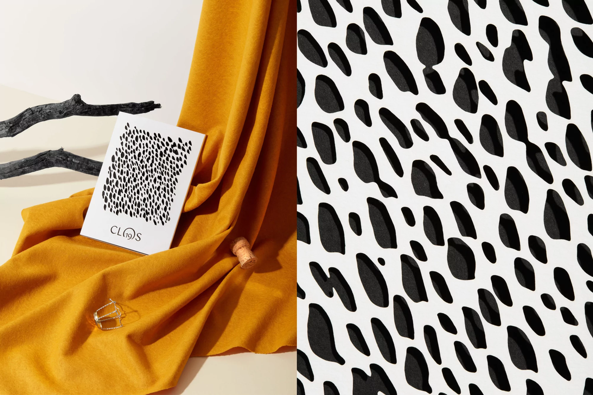 Elevated still life featuring mustard-yellow fabric, decorative branch, cork, metal buckle, and a white book with black abstract spots.