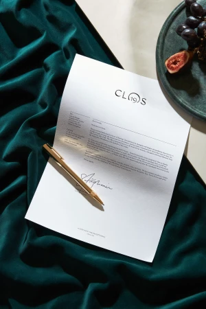 Close-up still life composition featuring a signed contract, golden pen, grapes, and figs on a green velvet surface.