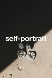 Crystal heart drop earrings displayed on a sandy surface with strong diagonal shadow casting