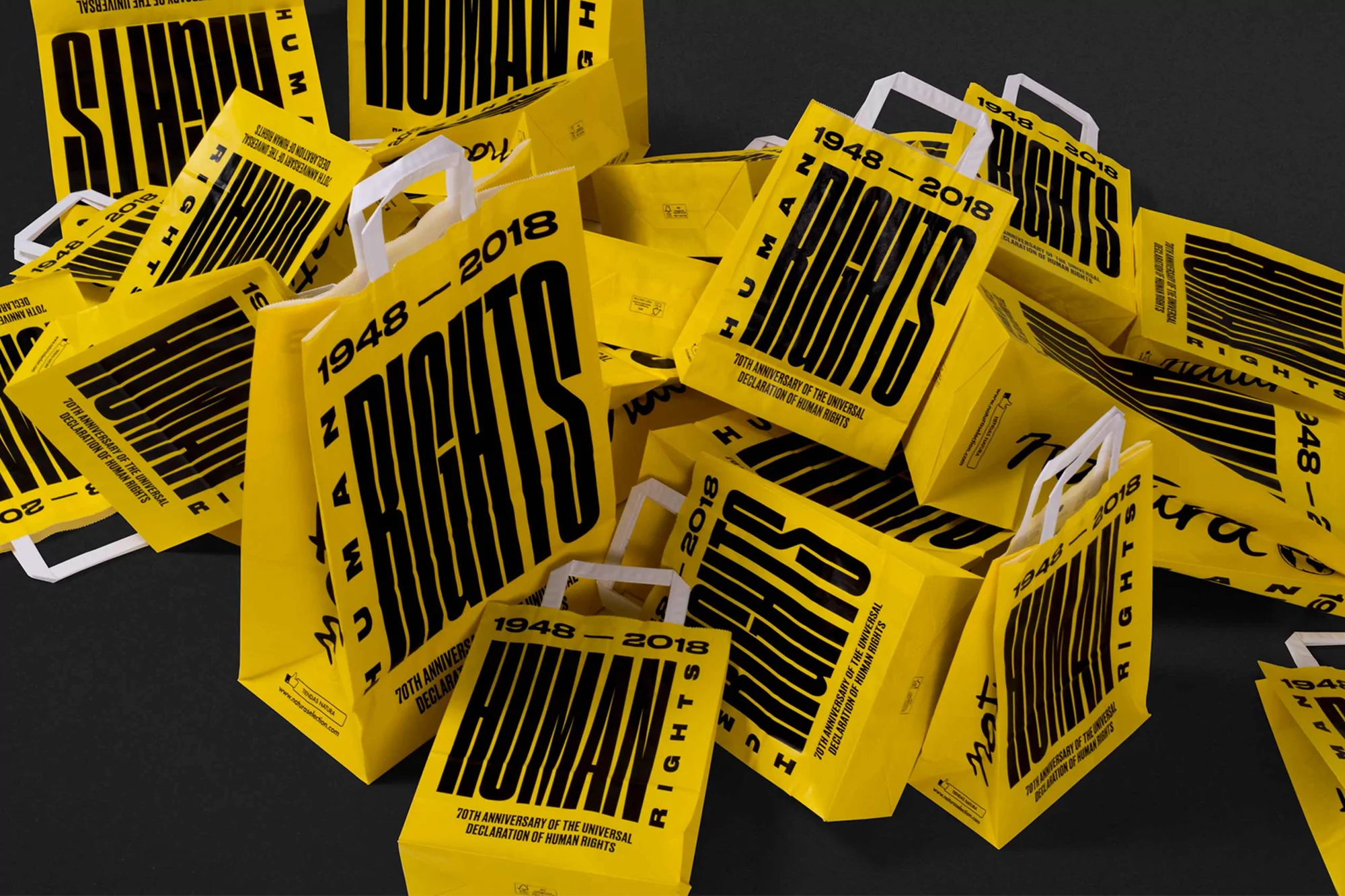 Pile of yellow shopping bags with black text "Human Rights 1948-2018" against a dark background, creating a visually striking graphic.