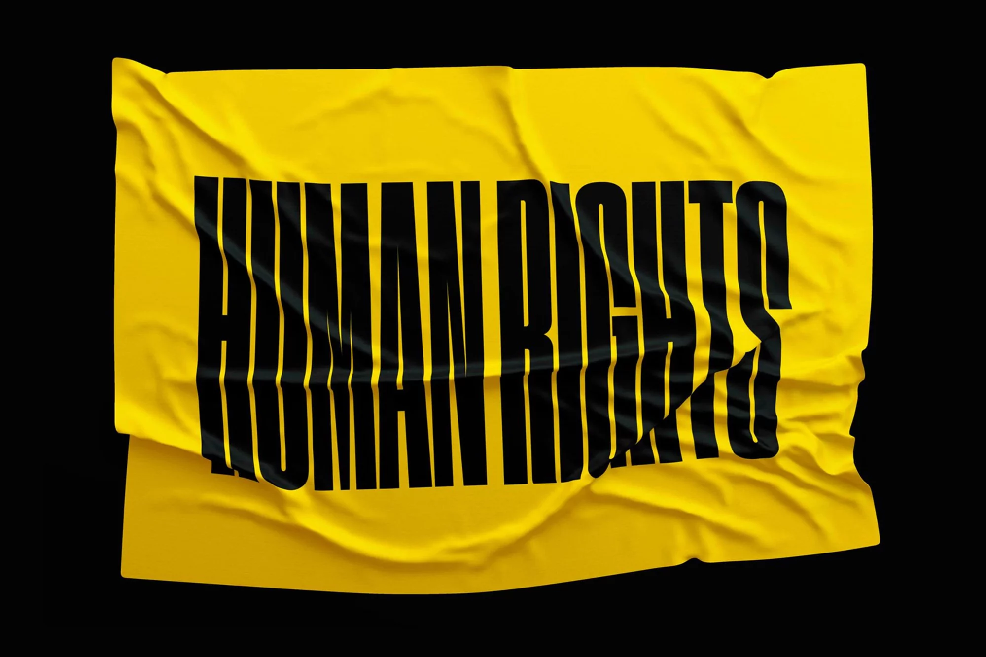 Wrinkled yellow fabric with bold black 'HUMAN RIGHTS' text against a black backdrop, simple studio shot for impactful visual communication.