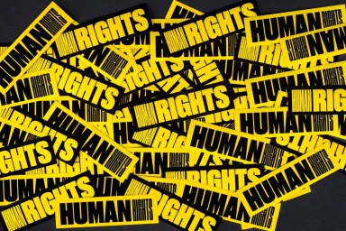 Collage of rectangular yellow stickers featuring bold black typography reading human rights scattered across a dark surface.