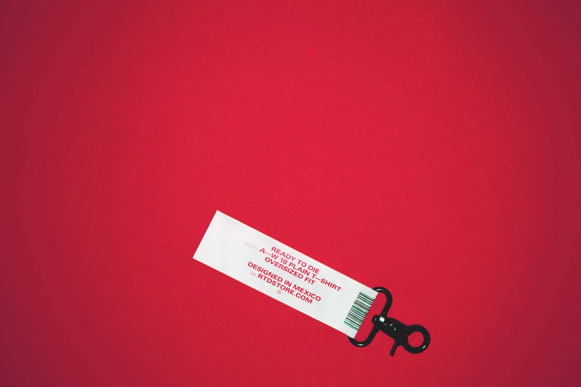 White clothing tag with black lanyard on red background, featuring fashion brand name, product type, and 'Designed in Mexico' text.