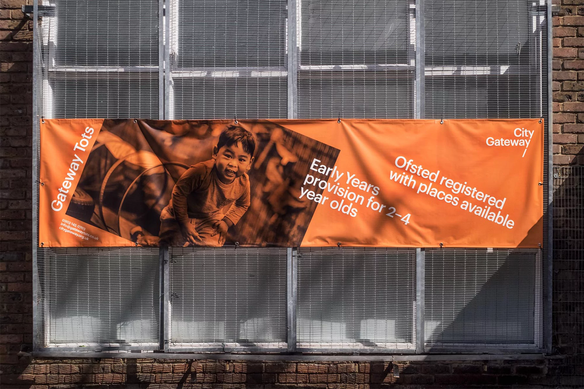 Eye-level shot of an orange banner with a child's image and white text attached to a window with brick and metal details.