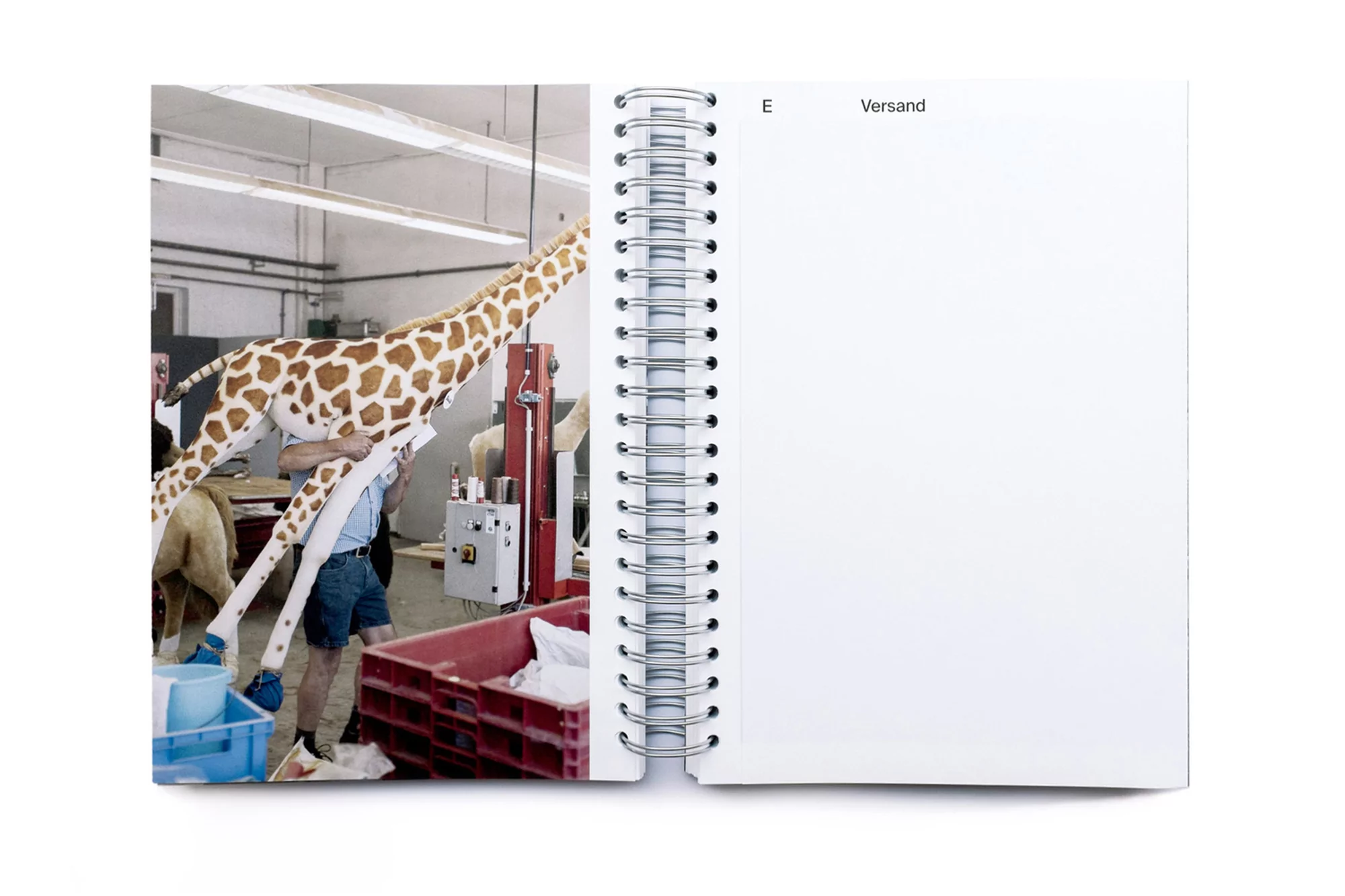 Open notebook displaying a giraffe prop being assembled in an industrial setting with visible workers and equipment, bright overhead lighting.