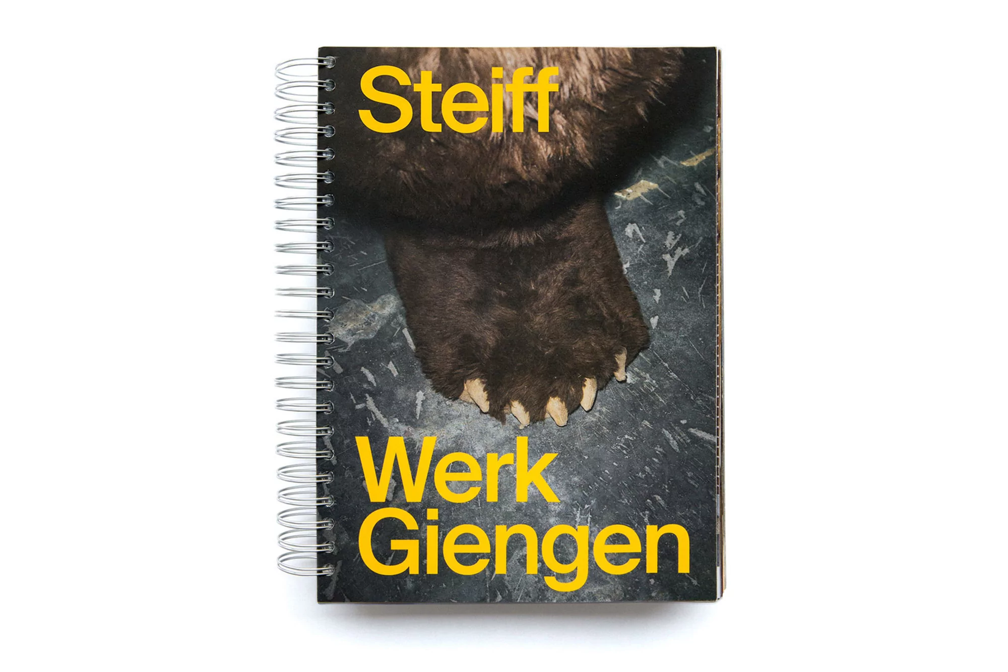 Steiff Werk Giengen spiral notebook with bear paw graphic on the cover, yellow text, isolated on white backdrop, studio photography.