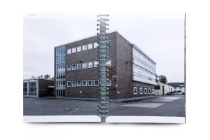 Open spiral-bound book displaying a photograph of a brick commercial building exterior with a paved courtyard