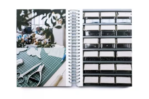 Open spiral-bound notebook showing workshop photos, cutting mat with scissors, and storage bins with labels.