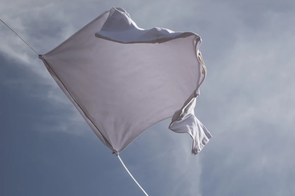 A white garment waves against a blue sky with light clouds, suggesting wind and movement in an outdoor setting with natural lighting.