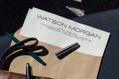 Watson Morgan brand stationery letter and brown paper envelope resting on textured fabric with pens