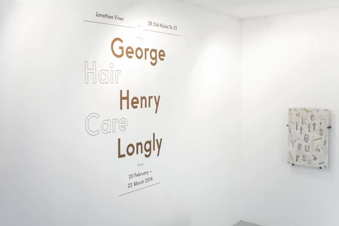 Art installation featuring typography on a white wall, including names and dates, in a minimalist gallery setting with natural lighting.
