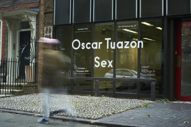 Exterior view of Jonathan Viner Gallery with exhibition typography on glass, cobbles in foreground and blurred walking figure