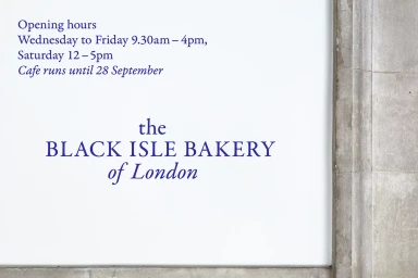Signage displaying opening hours and the Black Isle Bakery of London brand typography against a white wall.