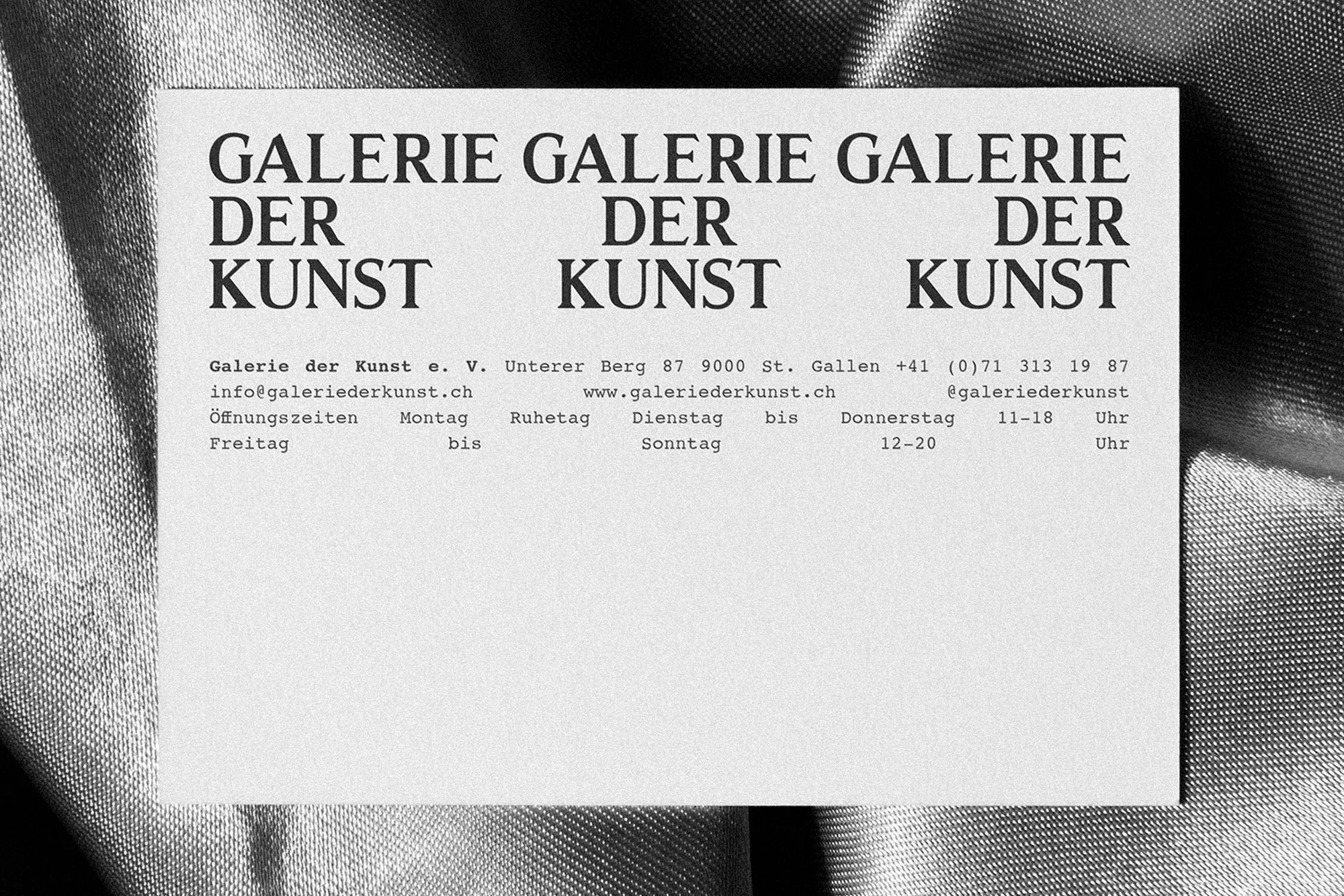 Monochrome business card featuring Galerie der Kunst branding resting on a textured fabric surface.