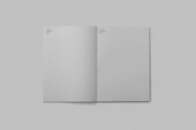 Open book spread on a neutral gray surface with text on each page, displaying typography examples with contrasting font styles.