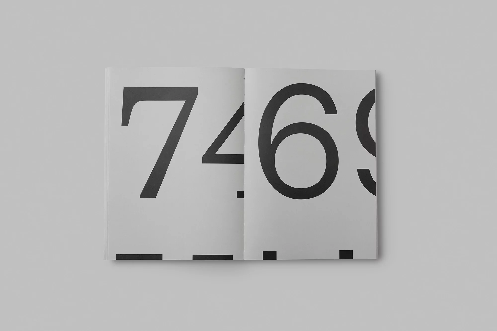 Open book displaying large black numbers '74' on the left page and '69' on the right page against a clean, light grey background.