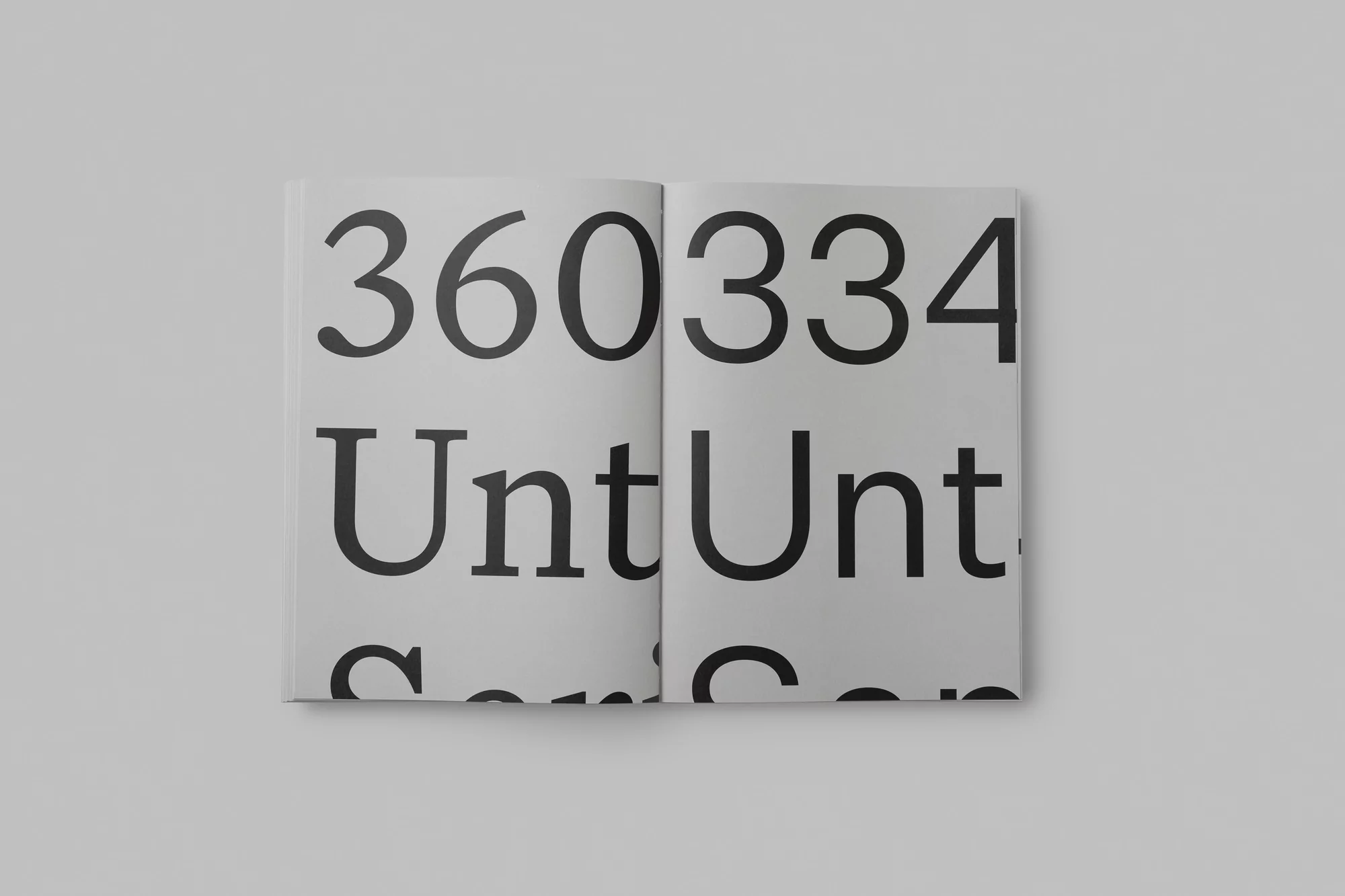 Opened book displays bold sans-serif typography spelling '360334 UntUnt.' on white pages, set against a plain light gray background.