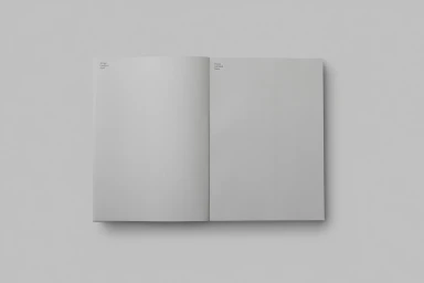 An open softcover book with blank light grey pages lying flat against a matching plain grey background surface