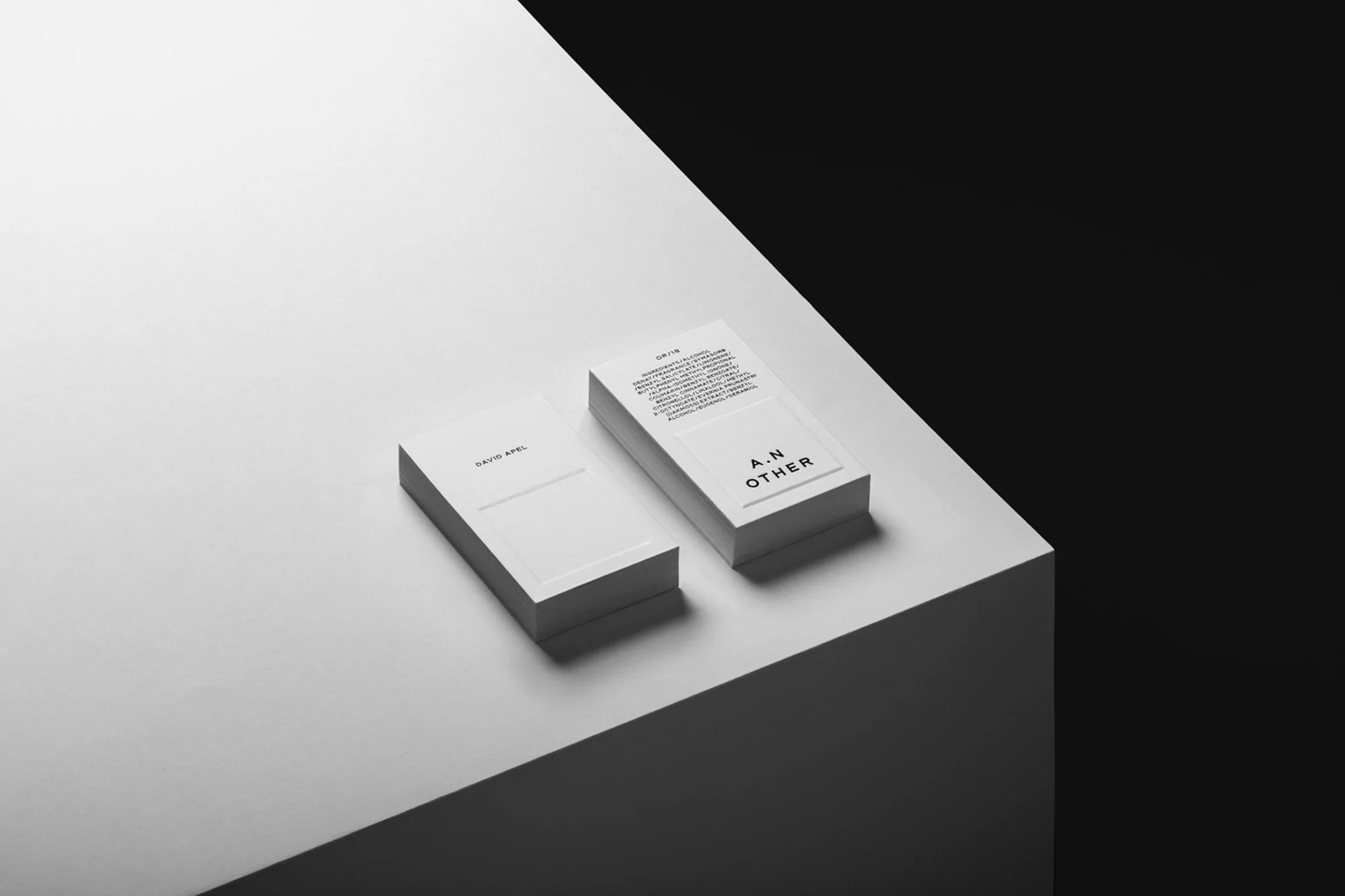 Two stacks of white business cards on a bright white surface, with a stark black background in a minimalist, high-contrast studio shot.