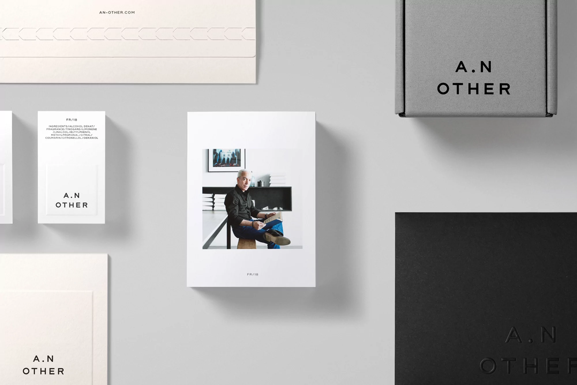 Still life of A.N OTHER brand packaging including a box, cards, and a photograph of a man in a modern interior space.