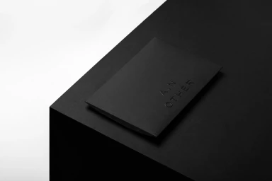 Black envelope with embossed text resting on a dark corner surface against a plain white background